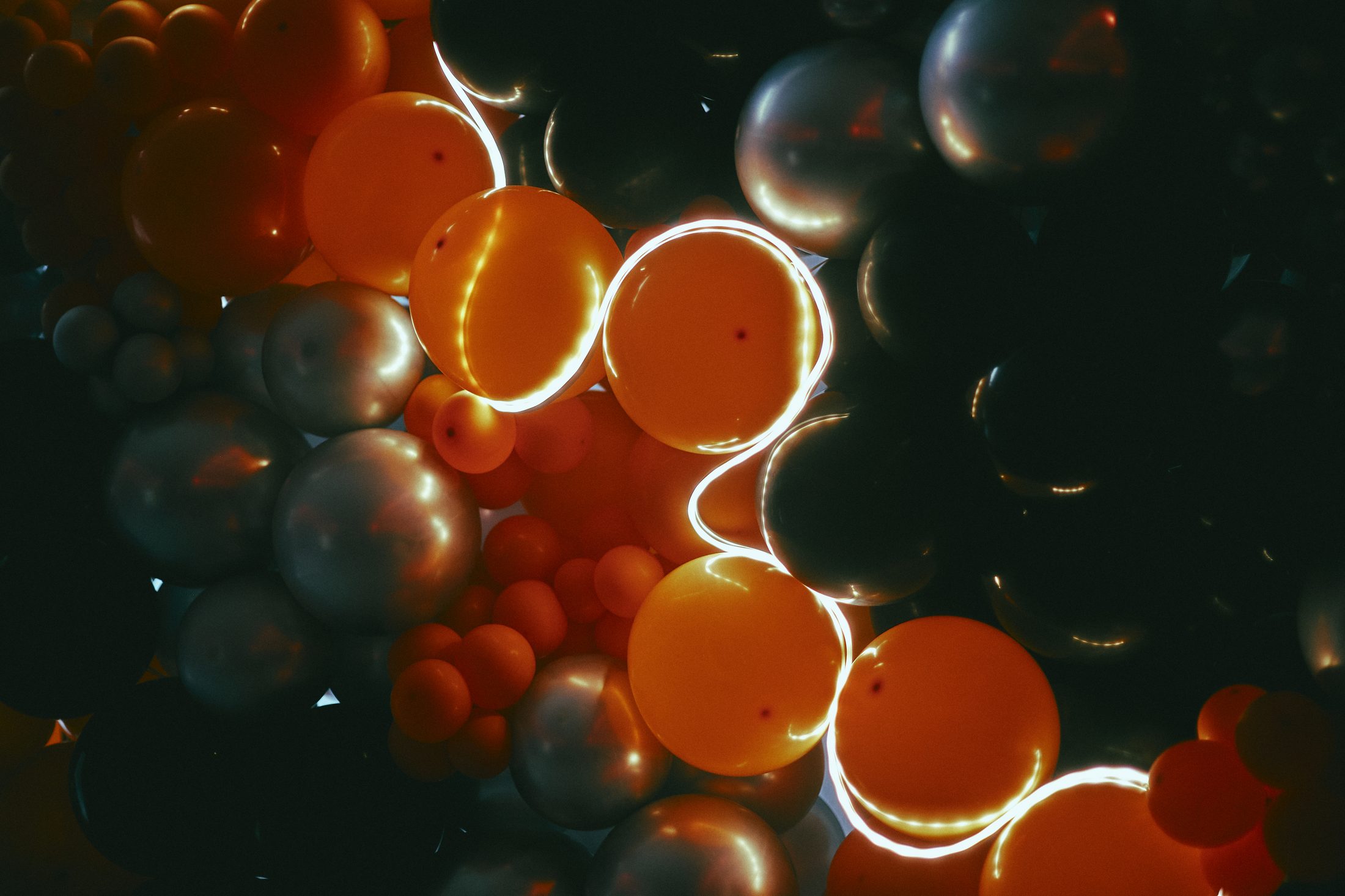 Enseigne au néon posée en diagonale sur un mur de ballons noirs et orange, allumée dans un hall en pénombre à Montréal